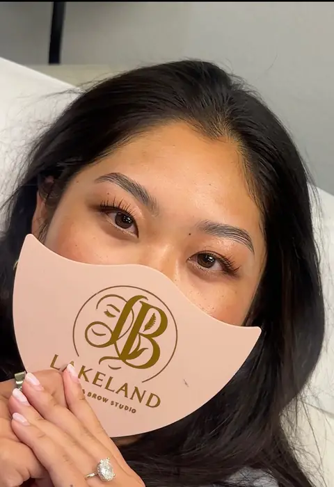 After: client holding a studio shield with laminated brows and lifted lashes