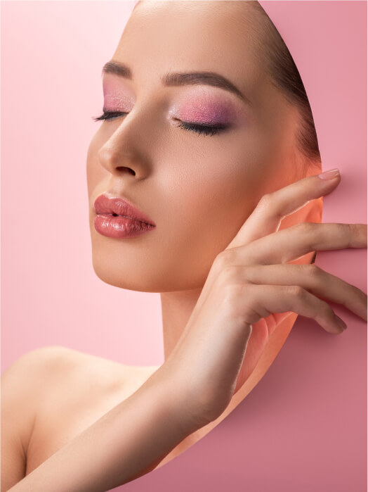 A woman with closed eyes and pink makeup poses against a pink background, gently touching a curved pink lakeland panel with her hand.
