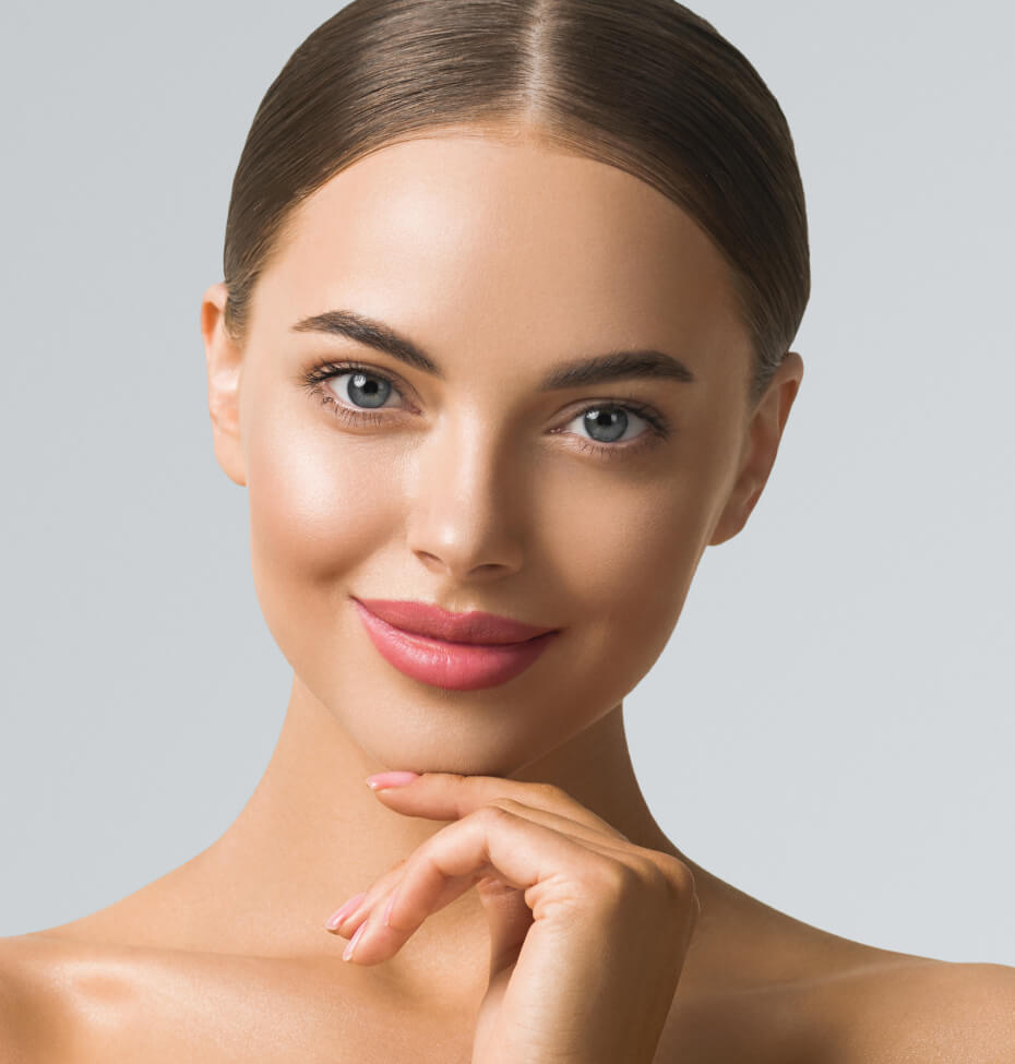 A young woman with smooth skin and neatly styled brown hair smiles slightly, resting her chin on her hand against a neutral lakeland background.
